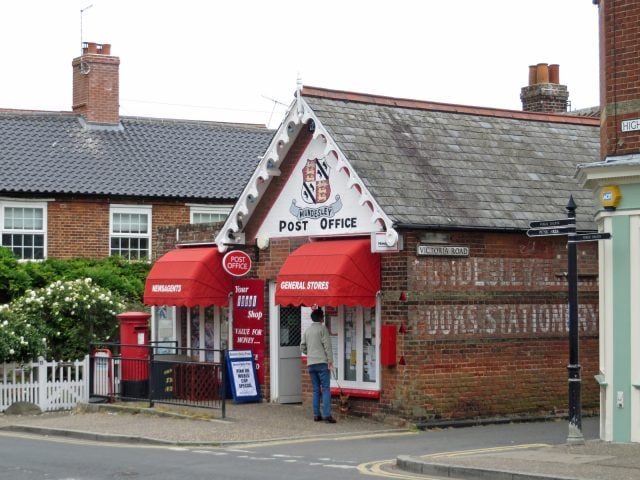 A village sub-post office in Mundesley, Norfolk, with Post Office signage, red awnings and a customer at the door