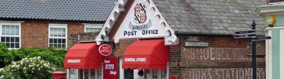 A village sub-post office in Mundesley, Norfolk, with Post Office signage, red awnings and a customer at the door