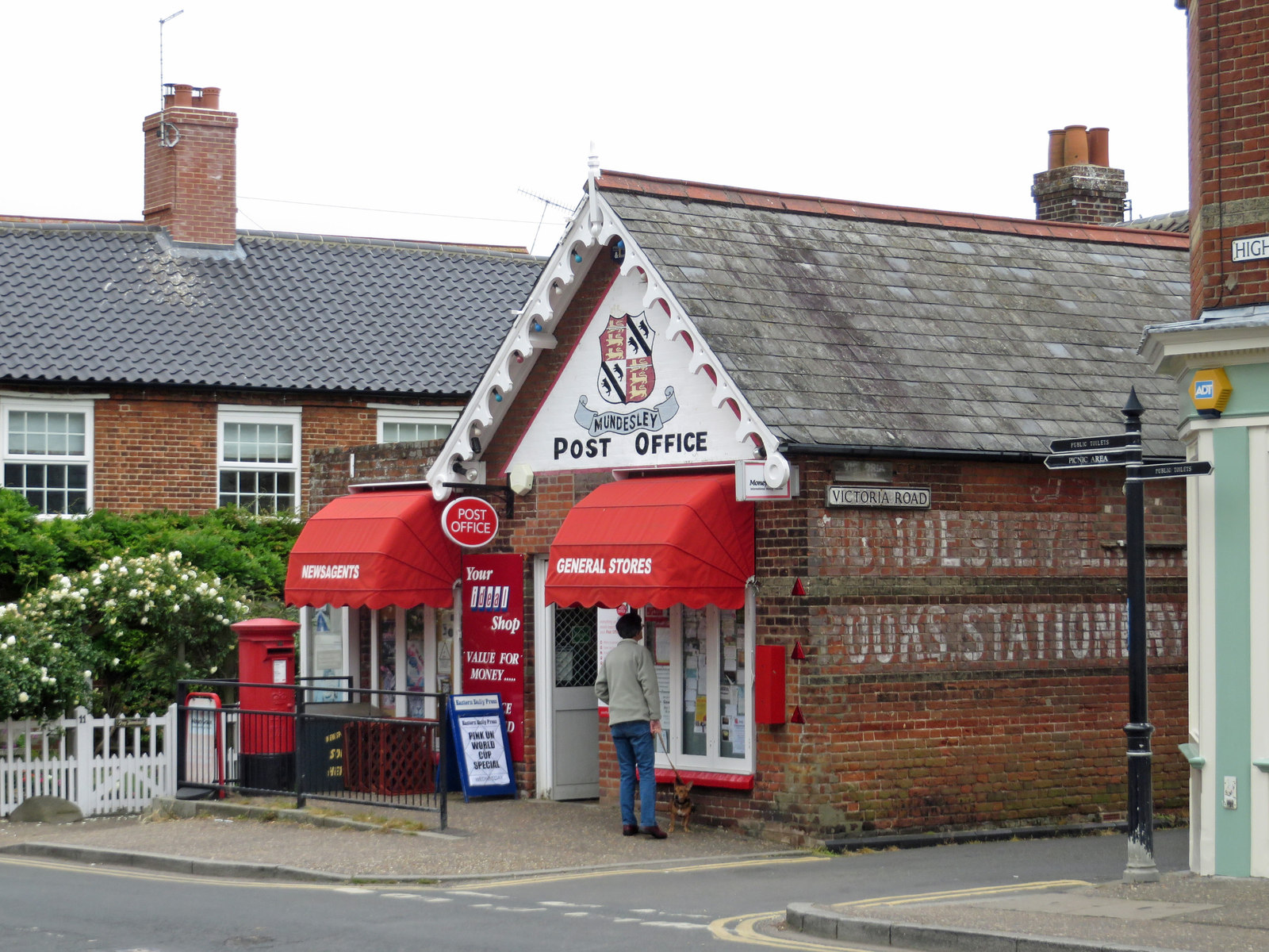 A village sub-post office in Mundesley, Norfolk, with Post Office signage, red awnings and a customer at the door